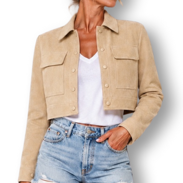 A woman modeling a cropped beige jacket over a white top and light blue denim shorts, standing against a plain white background.