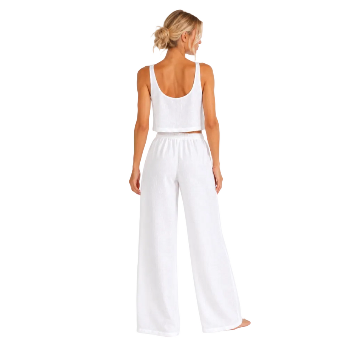 A woman shown from the back wearing a white two-piece lounge set consisting of a cropped tank top and wide-leg pants, photographed against a seamless white studio background.