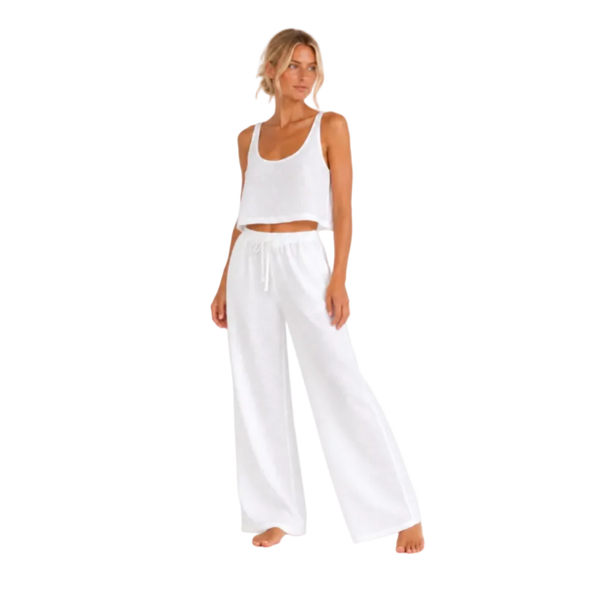 A woman modeling a white two-piece loungewear set consisting of a cropped tank top and wide-leg drawstring pants, photographed against a seamless white studio background.