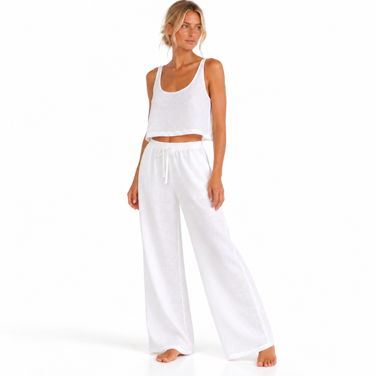 Angled view of a model wearing The Linen Travel Set by Hostess the label, with a white sleeveless crop top and wide-leg drawstring pants.