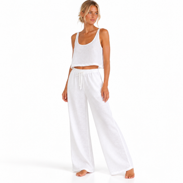 Angled view of a model wearing The Linen Travel Set by Hostess the label, with a white sleeveless crop top and wide-leg drawstring pants.