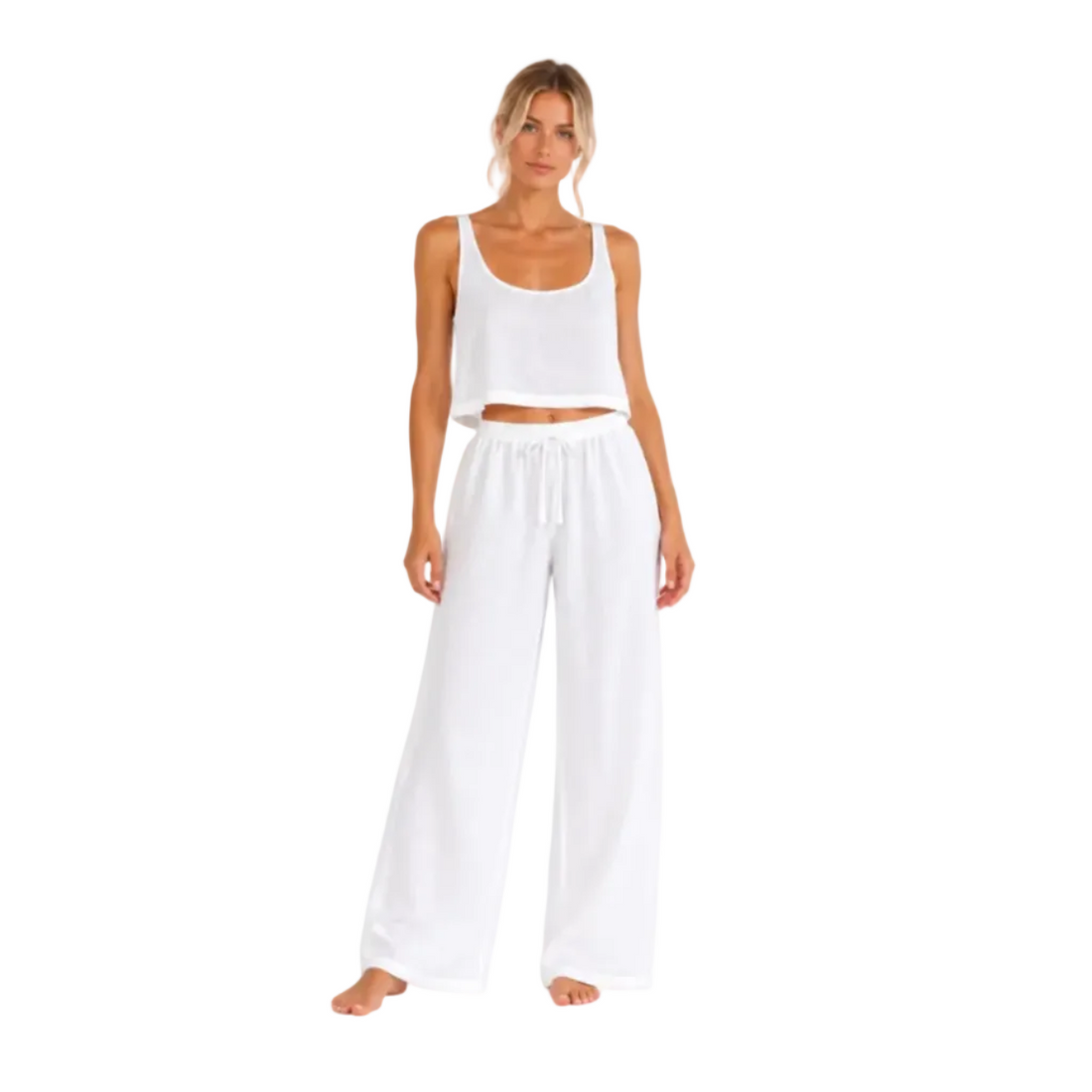 A woman modeling a white two-piece lounge set consisting of a cropped tank top and wide-leg drawstring pants, photographed against a seamless white background.