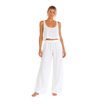 A woman modeling a white two-piece lounge set consisting of a cropped tank top and wide-leg drawstring pants, photographed against a seamless white background.